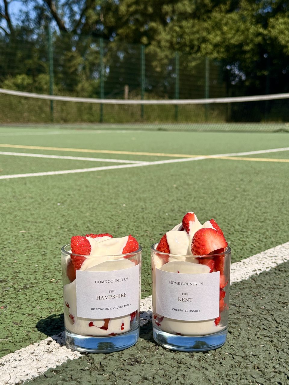 Two Home County Co. candles topped with strawberries and cream on the baseline of a tennis court